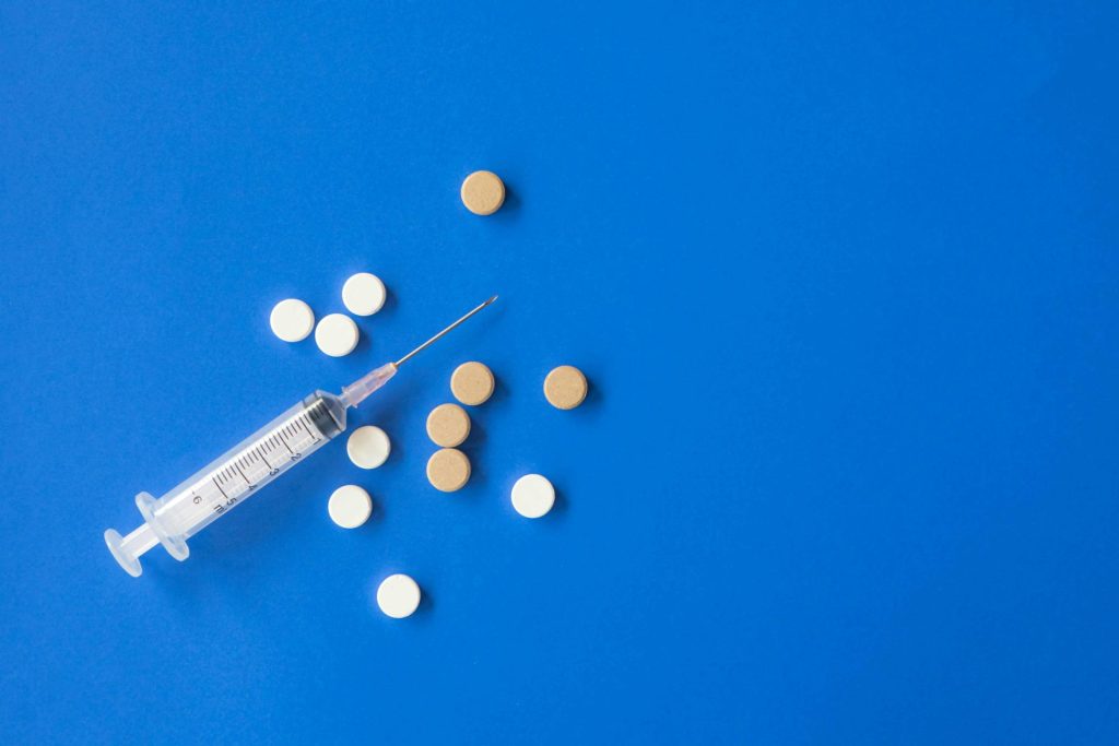 Top-view flat-lay composition featuring a Vitamin C medical syringe and various pills placed on a blue background.